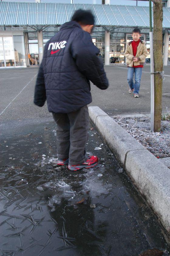 張っている氷を踏んで遊ぶ子どもの写真