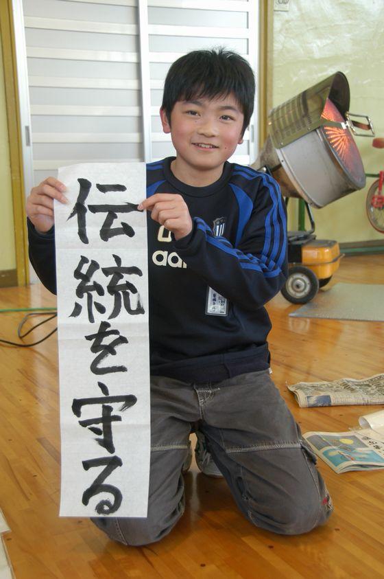 宮宿小書き初め大会で書いた「伝統を守る」を持ってこちらに見せている児童の写真