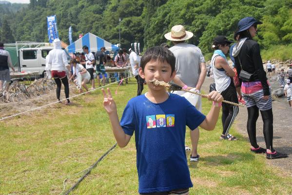 串に刺さった焼き魚を食べる子どもの画像