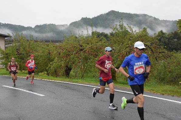 リンゴ畑を横目に走る選手たちの写真