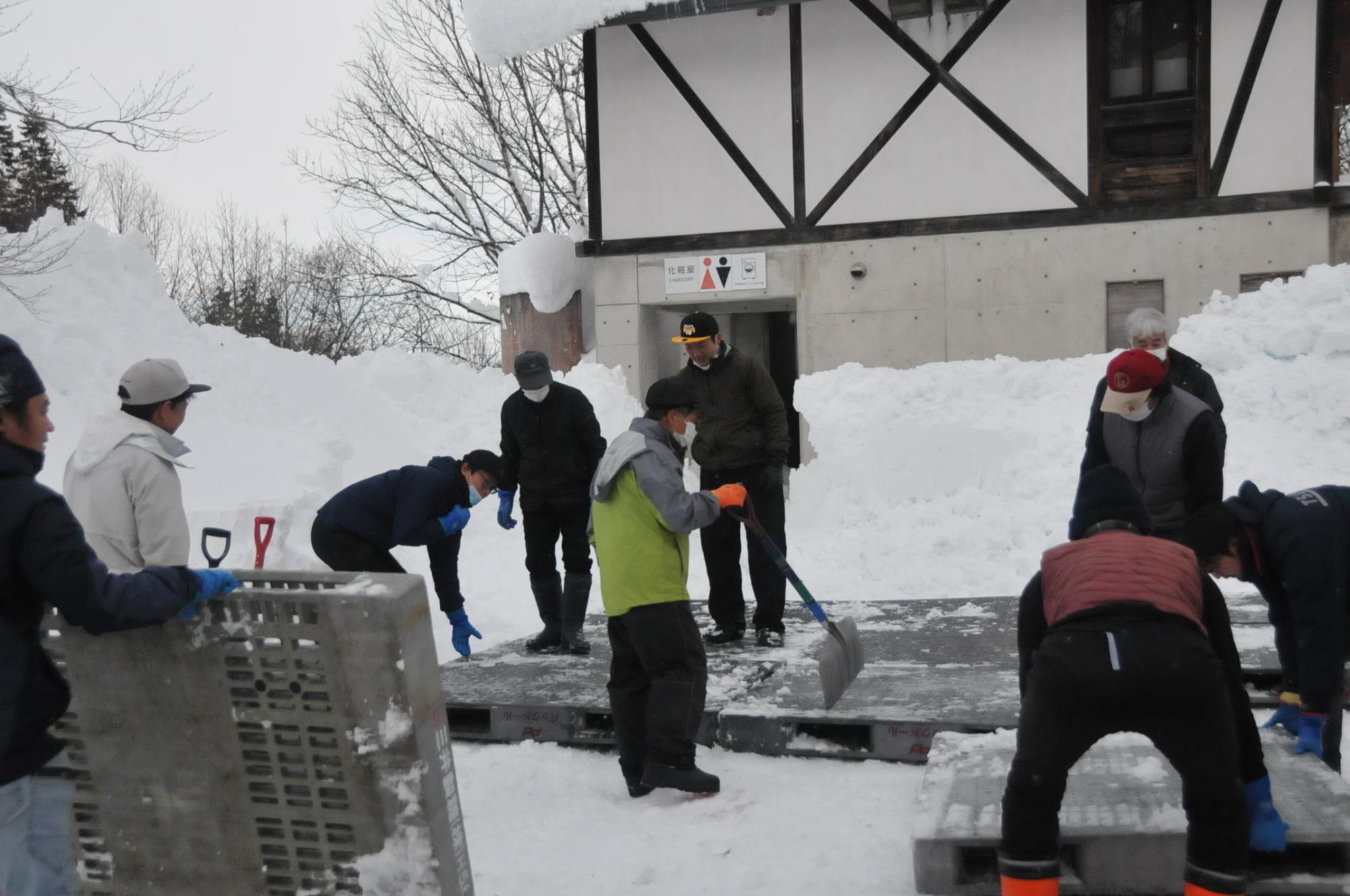 雪をならした場所にパレットを置く様子